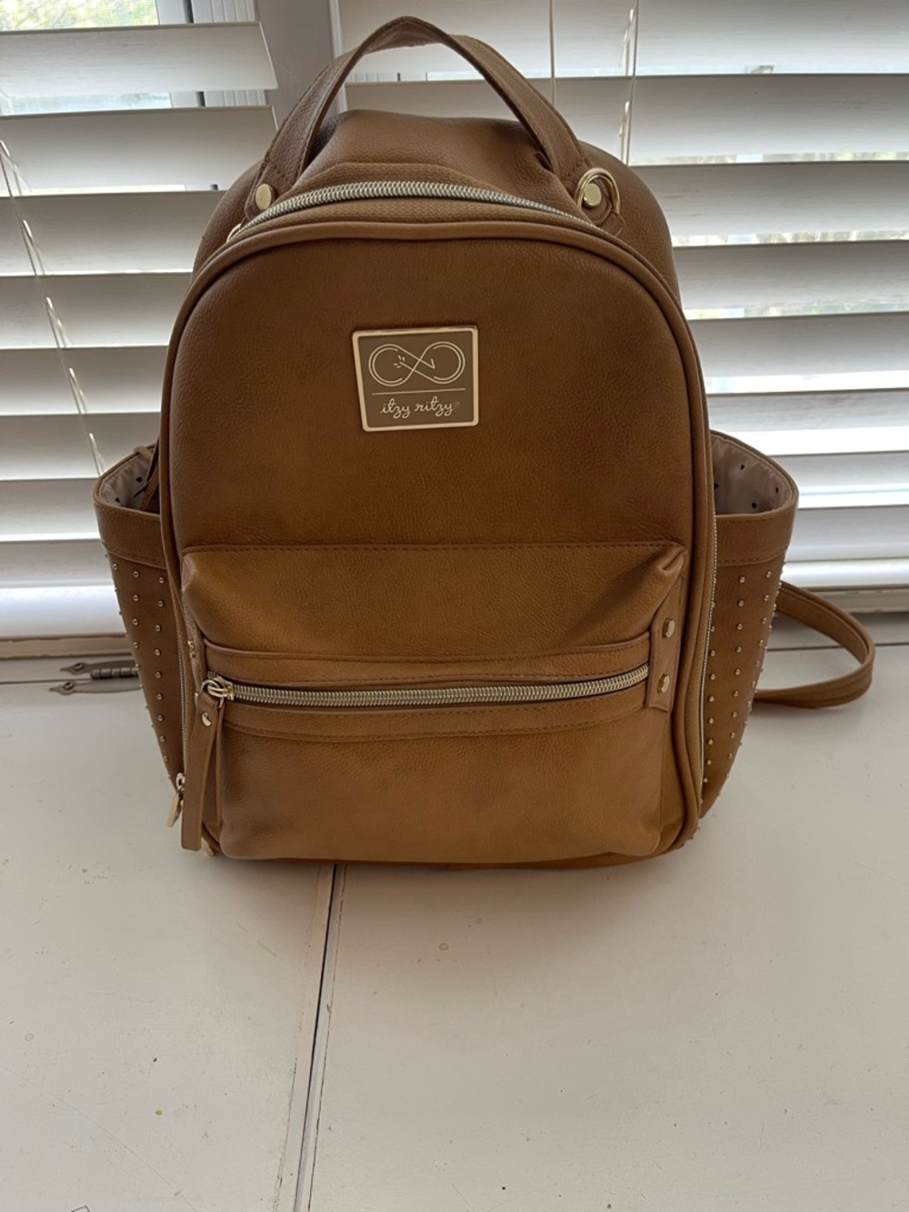 Itzy Ritzy Tan Faux-Leather Backpack with Gold Accents and studded pockets.